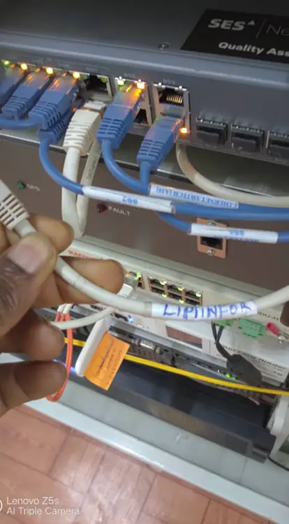 

This is a close-up photo of a technician's hand holding a white network cable in front of an active network switch in a server rack.